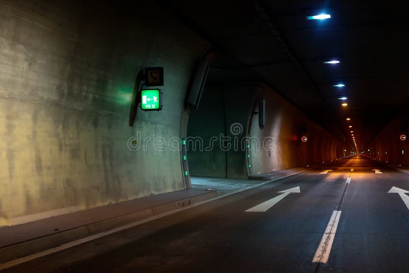 Automobile auto dark car tunnel with white arrows on asphalt showing way direction. Emergency exit sign with many lights. Empty underground vehicle road. Urban royalty free stock photos