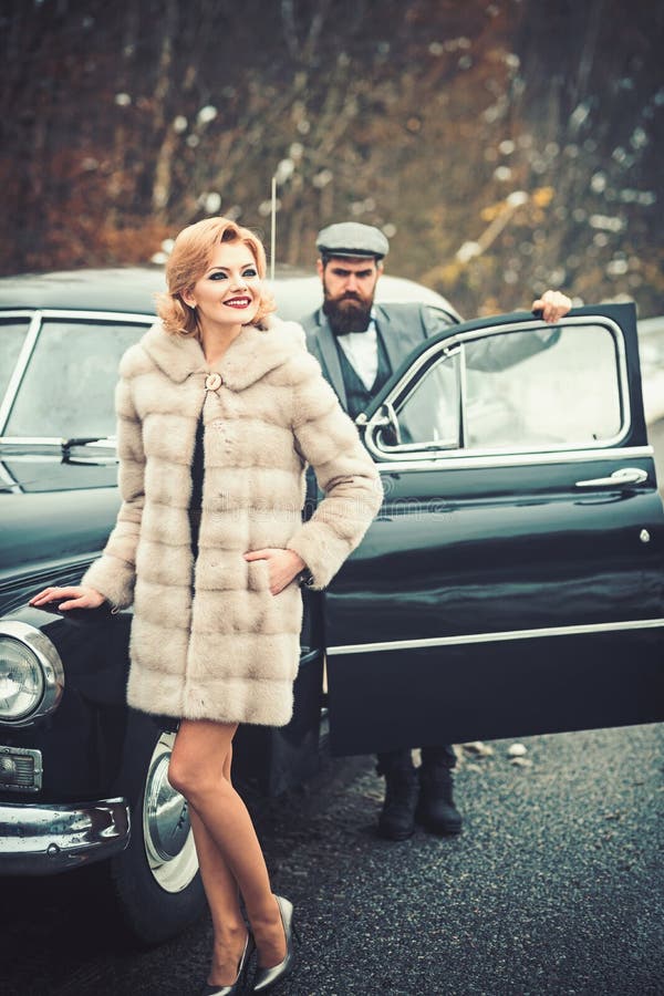 Bearded man and sexy woman in fur coat. Escort of girl by security. Retro collection car and auto repair by mechanic. Bearded men and sexy women in fur coat stock photography