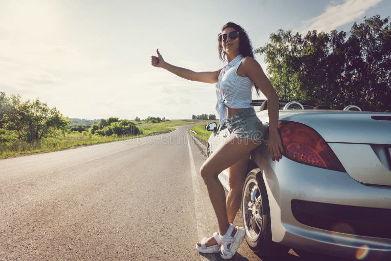 Beautiful woman hitchhiking by a broken car. beautiful young sexy girl in short shorts stands at her convertible. Problems with. Beautiful woman hitchhiking by a royalty free stock photography