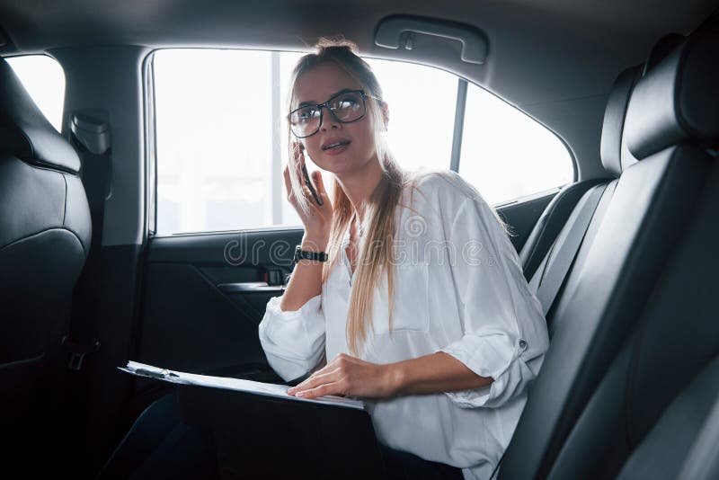 Busy girl. Smart businesswoman sits at backseat of the luxury car with black interior.  royalty free stock photo