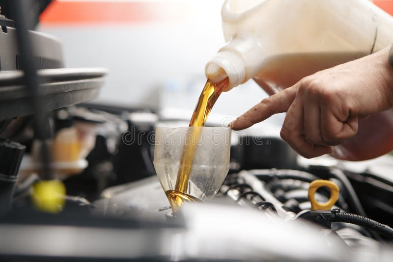 Car mechanic replacing and pouring fresh oil into engine at maintenance repair service station stock images