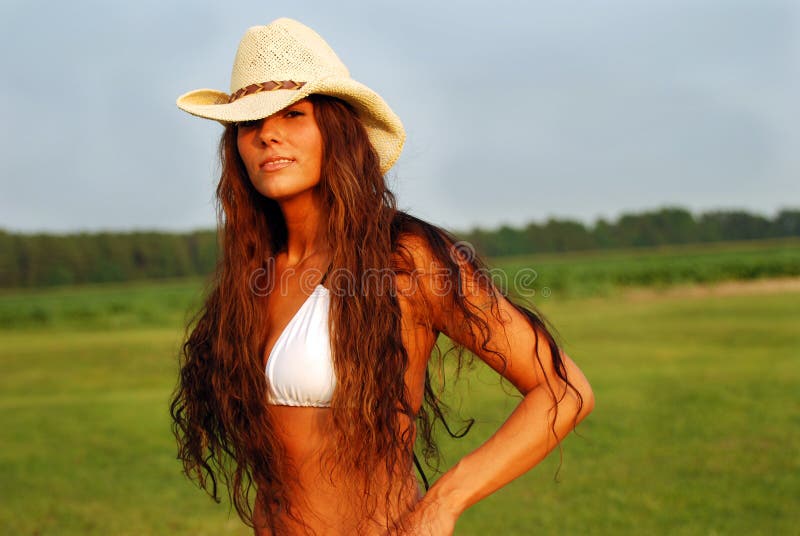 Country girl long hair. Girl with long hair and cowboy hat looks into the camrea near sunset with field and young cornfield in background royalty free stock photography