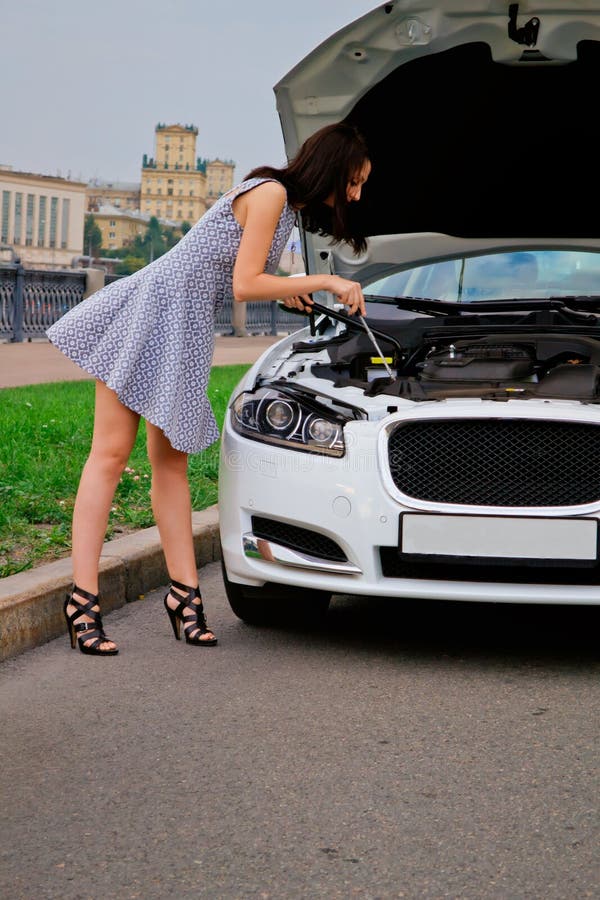 Cute brunette and luxury car. Cute brunette with red lips on high heels is posing with luxury white car (Jaguar XF) outdoor. Repairing car