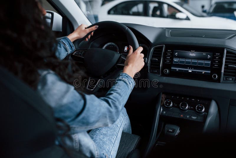 Different buttons and knobs. Cute girl with black hair trying her brand new expensive car in the automobile salon.  royalty free stock images
