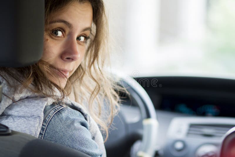 Girl driving car. Young woman behind driver`s seat looking at ca. R`s rear seat royalty free stock images