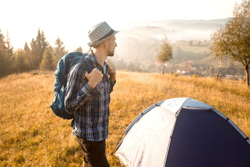 Handsome bearded man tourist exploring new places on top of mountains. Hiker man in hat with backpack happy to see sunrise. Handsome bearded man tourist stock image