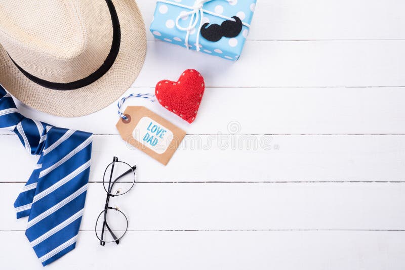 Happy fathers day concept. Top view of blue tie, beautiful gift box, man hat with glasses and retro film camera on white wooden. Table background. Flat lay royalty free stock photography