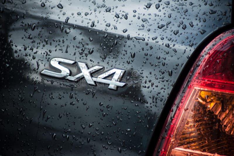 rain drops on black Suzuki SX4 rear logo parked in the street stock image