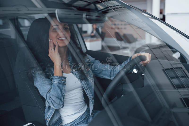 Not bad at all. Cute girl with black hair trying her brand new expensive car in the automobile salon.  stock photo