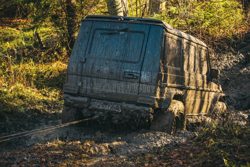 Off road car going through mud in forest. SUV stuck on country road with nature on background. Dirty offroad car needs help. Adventure, extreme driving and stock photo