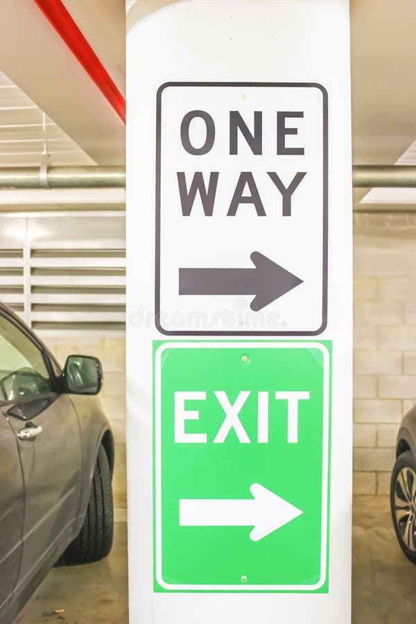 One way and exit signs on pillar in parking garage with parked cars to either side - close-up an selective focus.  royalty free stock photos