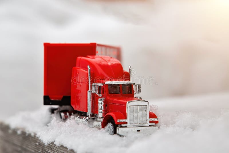Red toy truck rides on a winter snowy road. Wood flooring. Front view, close-up of a cargo tractor royalty free stock photo