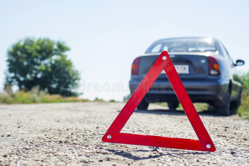 Red warning triangle with a broken down car. Red emergency stop sign and broken car on the road.  stock photo