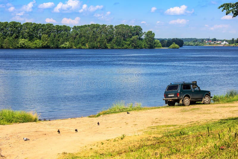 Russia, Uglich, July 2020. Lonely car on the beach near the Volga river. Small SUV on the yellow sand of the coastal beach, going to the wide river, blue water stock photo