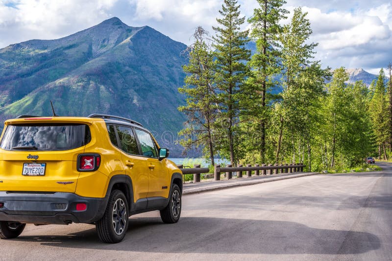 West Glacier, Montana/USA – July, 18 2019: Yellow Jeep parked along the Going to the Sun road in Glacier National Park with. Mountain range in background royalty free stock images