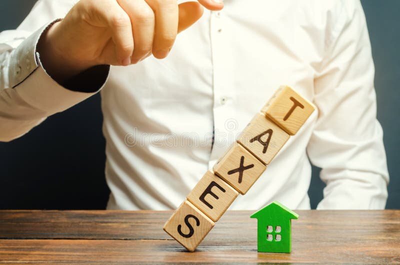 Wooden blocks with the word Taxes fall on a miniature house. The concept of the tax burden on housing, apartment, property. Mortgage. Taxation. Taxpayer stock image