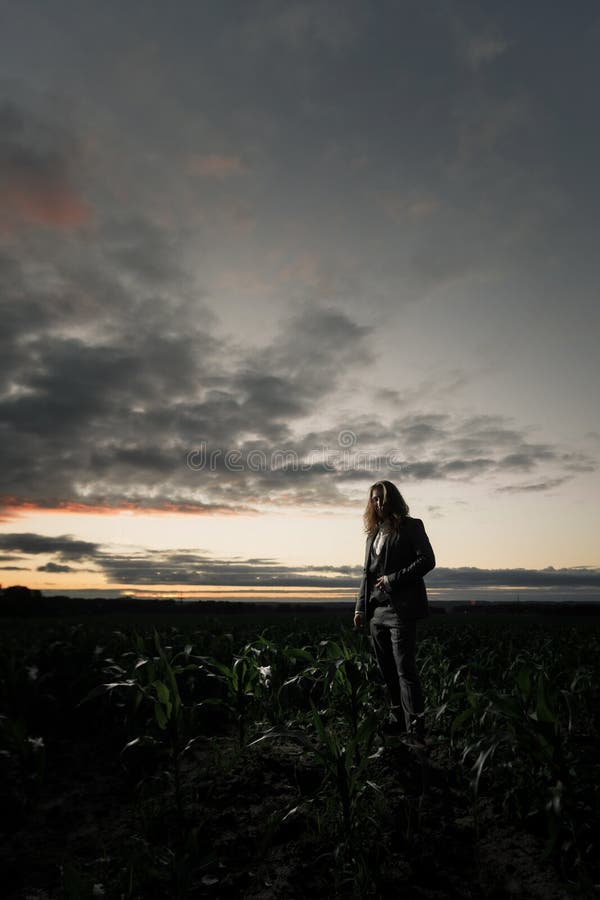 Young businessman stands in a field in a gray suit at sunset. Blond with long hair in a cornfield royalty free stock photography